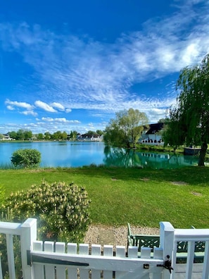 Un lago con una zona cubierta de césped, una valla blanca y un edificio al fondo.