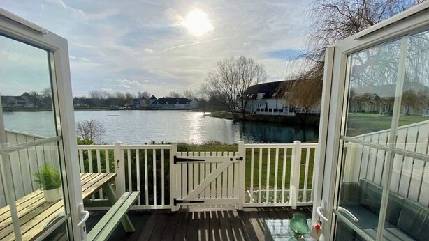 Eine Terrasse mit Blick auf einen See, ein weißer Zaun und eine Bank.