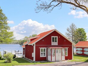 Un bâtiment rouge avec une porte et des fenêtres blanches, un porche couvert et un lac en arrière-plan.