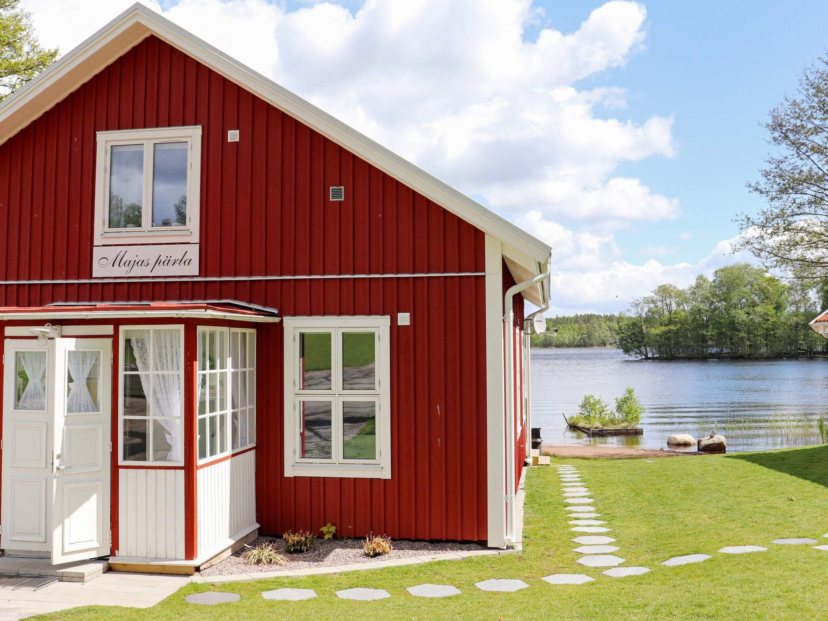 Een rood gebouw met een witte deur en ramen, een klein terras en uitzicht op een meer.