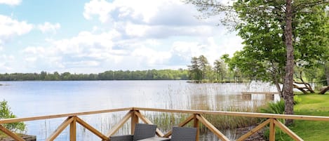 A deck with wicker furniture and a table, overlooking a lake.