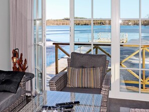 A room with a large window overlooking a frozen lake, a wicker sofa, a glass table with remote controls, and a decorative wooden sculpture. - 5 Star Holiday Home in Unnaryd (Unnaryd)