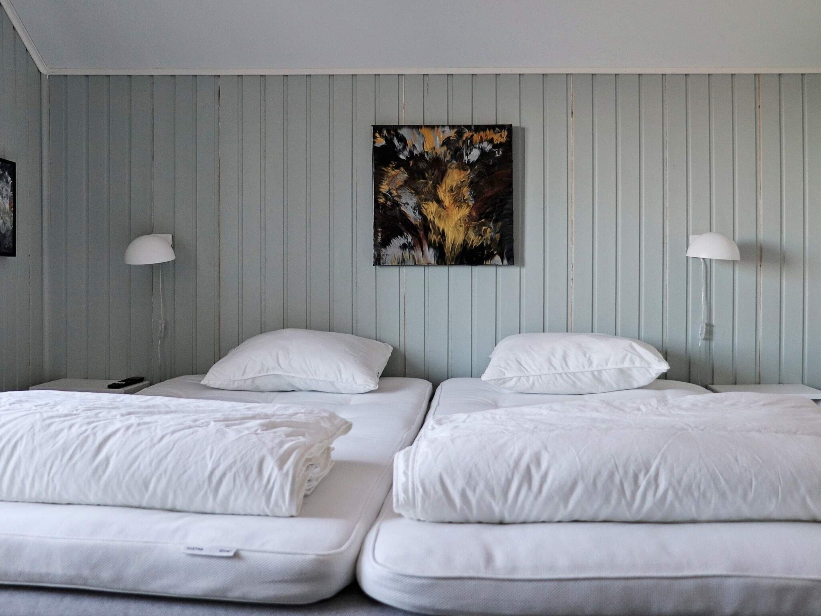 A room with two beds, each with white bedding and pillows, and a single painting on the wall.