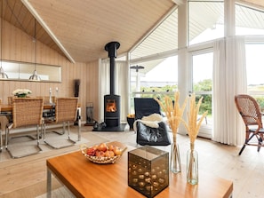 Un salon chaleureux avec une cheminée, des meubles en osier et une vue sur la verdure environnante.