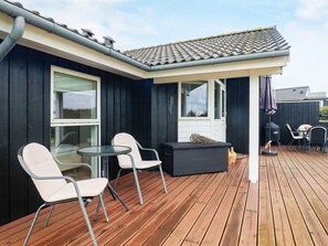 A covered outdoor seating area with two chairs and a table, a barbecue grill, and a wooden deck. - 8 Person Holiday Home in Lokken (Lokken)