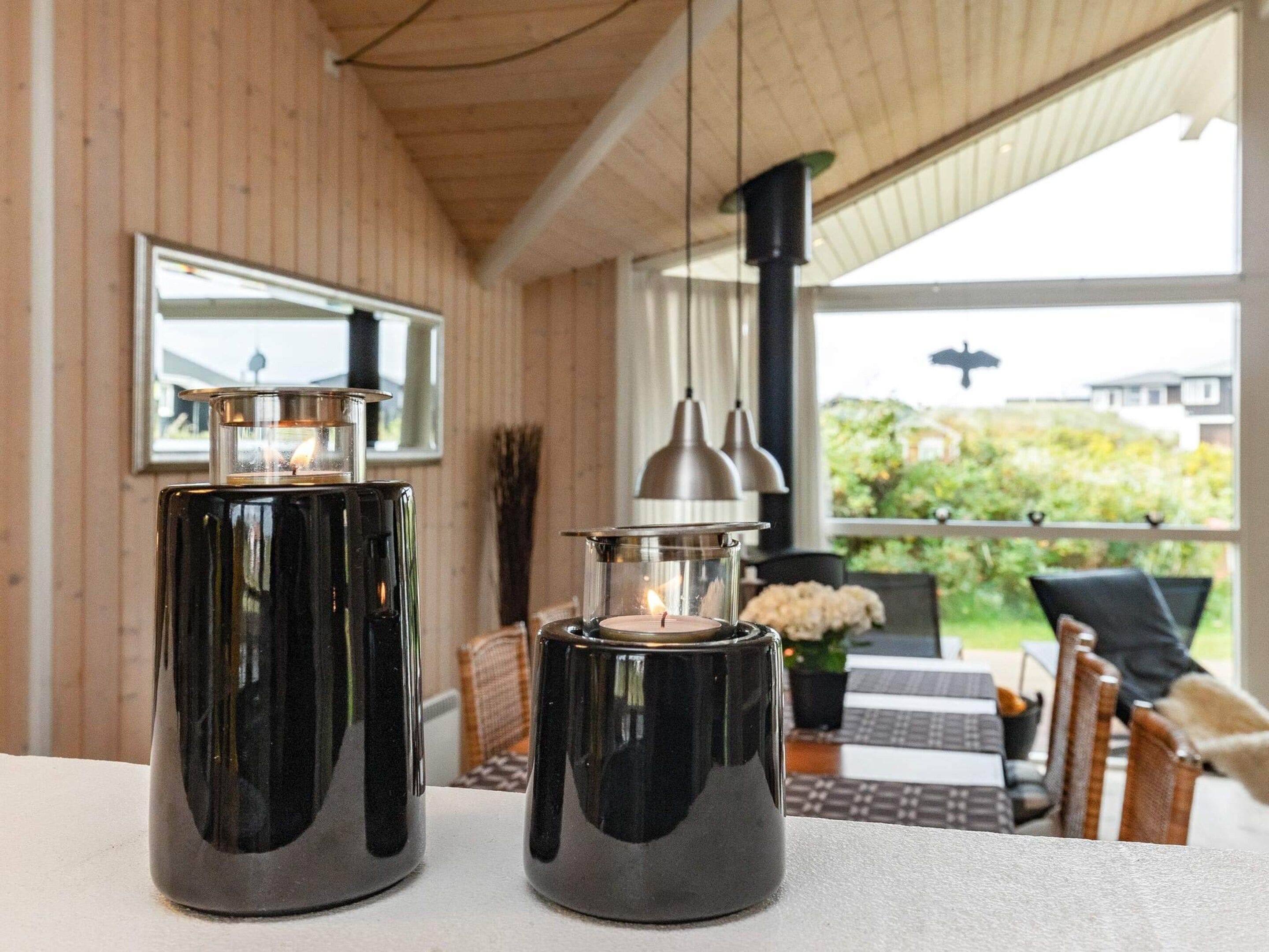 Two black candle holders on a table with a view of a garden and a house in the background.