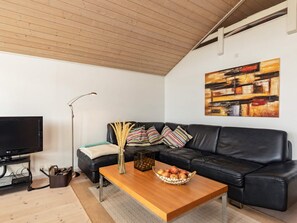A modern living room with a black leather sofa, a wooden coffee table with a basket of apples, a floor lamp, and a flat-screen TV.