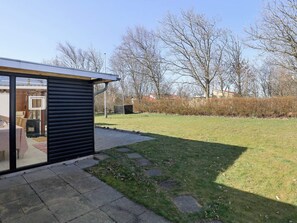 Ein moderner Außenbereich mit Terrasse, einer kleinen überdachten Sitzecke und einem Rasen.