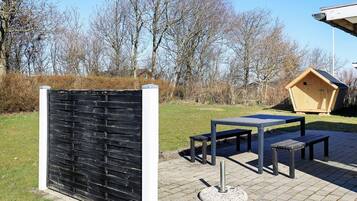 An outdoor seating area with a table and benches, a wooden structure, and a black fence.