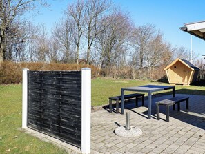 Et udendørs opholdsområde med borde og bænke, en trækonstruktion og et sort hegn.