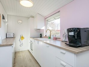A modern kitchen with white cabinetry, a wooden countertop, a coffee machine, and a window with a view of trees.