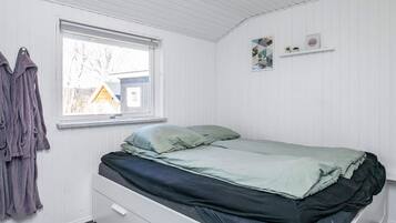 Un dormitorio con una cama individual, una ventana, un estante en la pared con dos objetos y una puerta.