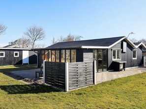 Et moderne hus med et stort glasparti, en træterrasse og en belagt indkørsel.