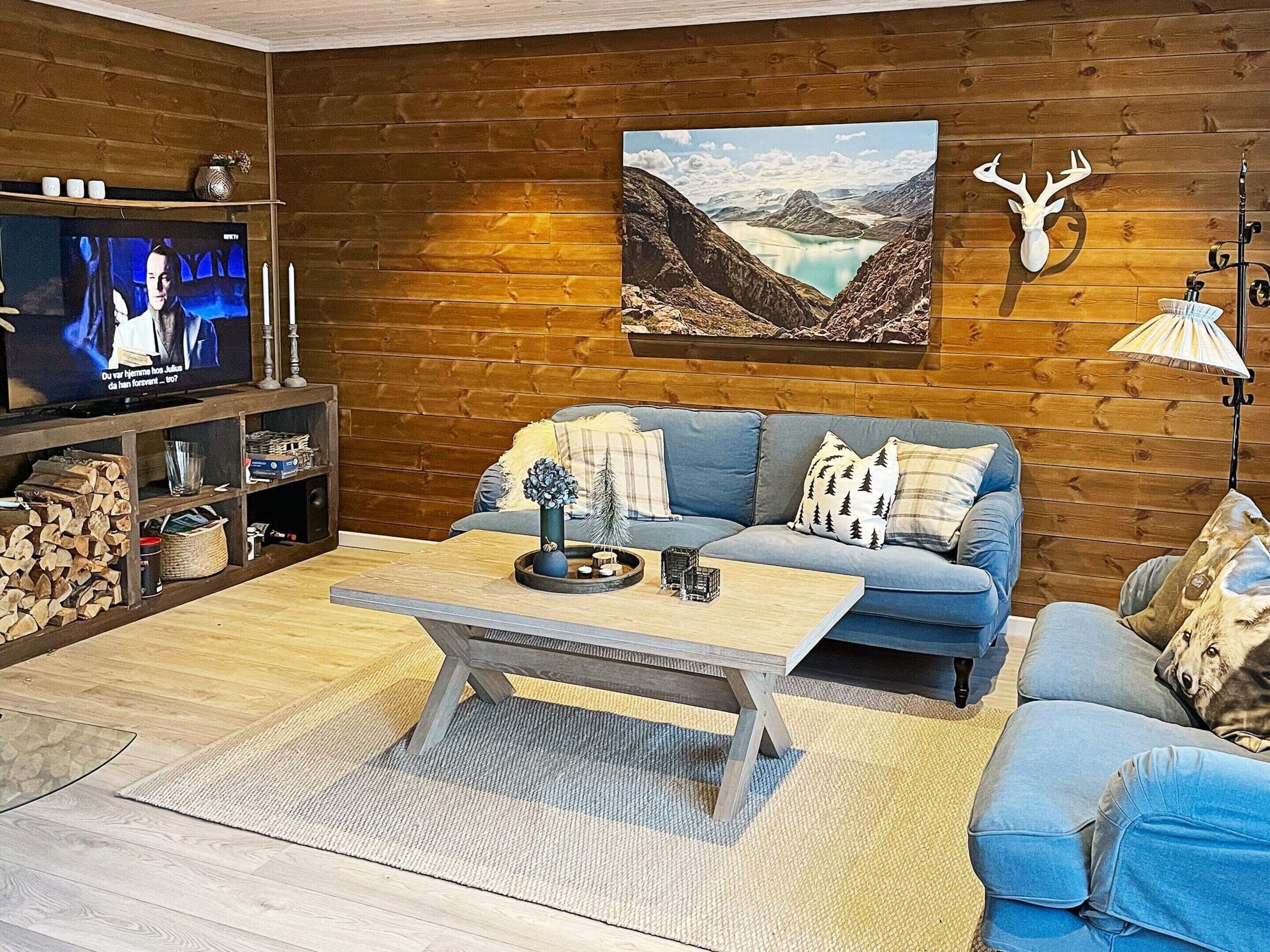 A cozy living room with a blue sofa, a coffee table, and a television on a wooden wall.