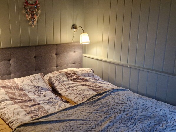 A bedroom with a tufted headboard, a patterned bedspread, and a wall-mounted lamp. - 4 Person Holiday Home in Sorstraumen (Kvaenangen)
