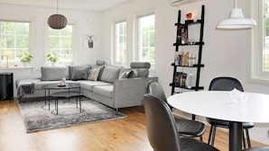 Una sala de estar moderna con un sofá gris, una mesa de centro redonda y un comedor con una mesa blanca y sillas negras.