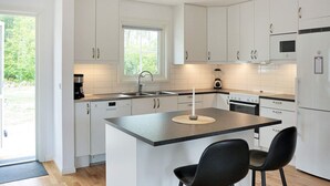 Una cocina moderna con armarios blancos, una isla central con dos sillas, horno empotrado y refrigerador.