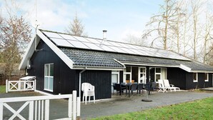 A black building with a sloped roof, solar panels, and a white fence.