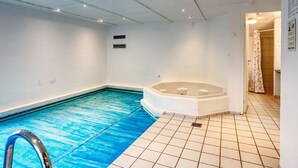 A swimming pool with a jacuzzi, tiled floor, and a shower area.