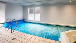 An indoor swimming pool with a view of trees outside, a window, and a tiled floor.