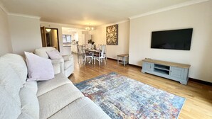 Een ruime woonkamer met een grote bank, een eethoek en een aan de muur bevestigde televisie.