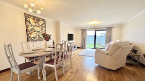 Een eetruimte met een houten tafel en stoelen, een schilderij aan de muur en uitzicht op de achtertuin door een schuifdeur van glas.