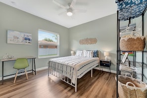 Une chambre à coucher comprenant un lit, un bureau, une chaise, une fenêtre et un ventilateur de plafond.