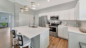 Una cocina moderna con armarios blancos, electrodomésticos de acero inoxidable y una isla central con taburetes de bar.