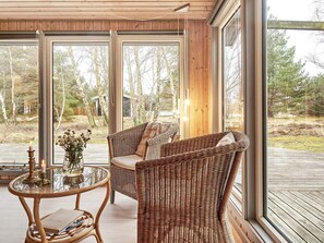 A cozy room with wicker furniture, large windows, and a wooden deck. - 4 Person Holiday Home in Aakirkeby (Akirkeby)
