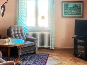 A living room with a sofa, a table, a radiator, a TV stand, and a window with curtains. - 7 Person Holiday Home in Oxaback (Öxabäck)