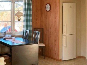 Une cuisine avec un mur en bois, un réfrigérateur blanc, une horloge et une fenêtre avec un rideau.