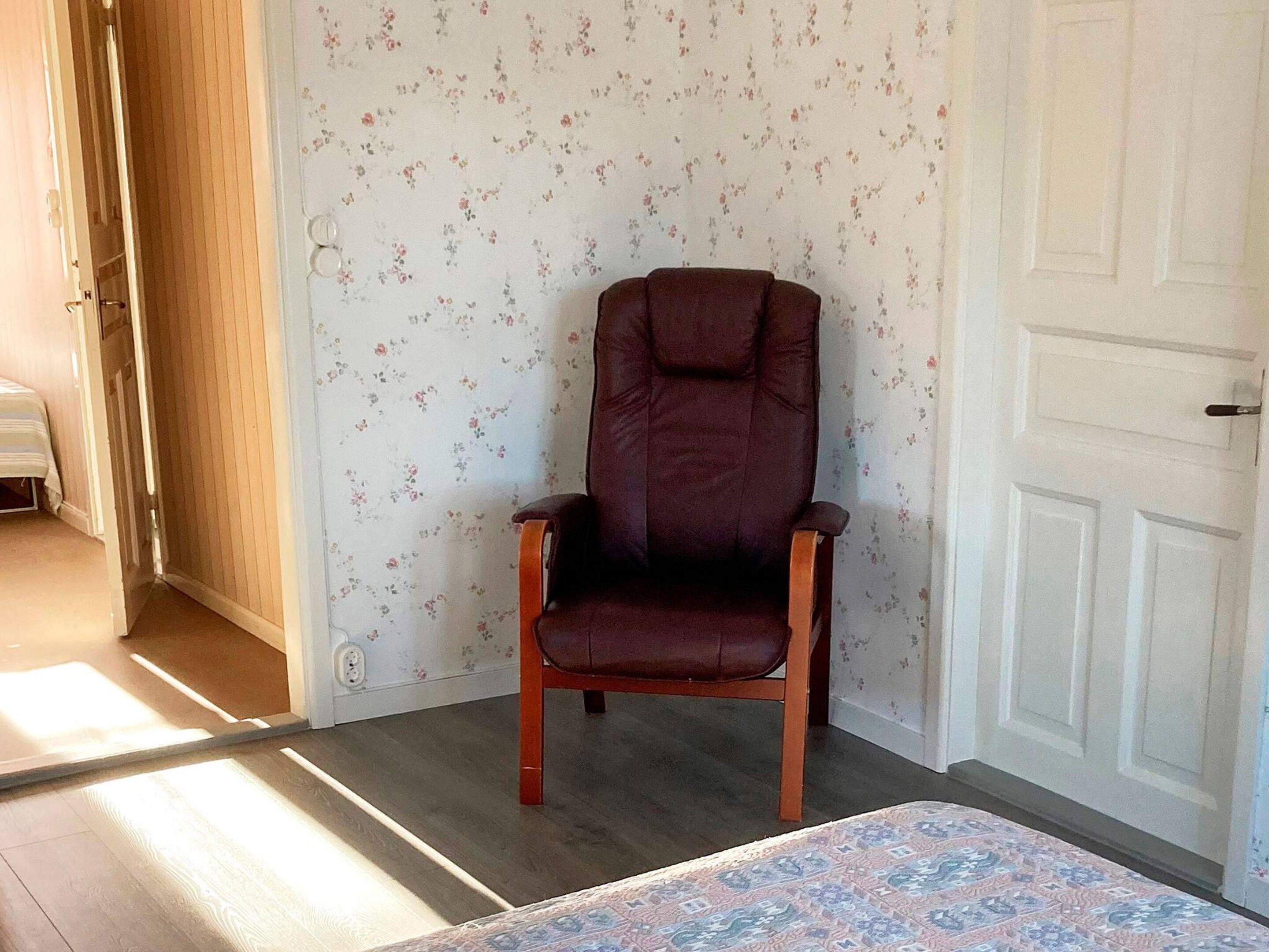 A room with a wooden floor, a floral wallpaper, a brown leather chair, and a patterned rug.