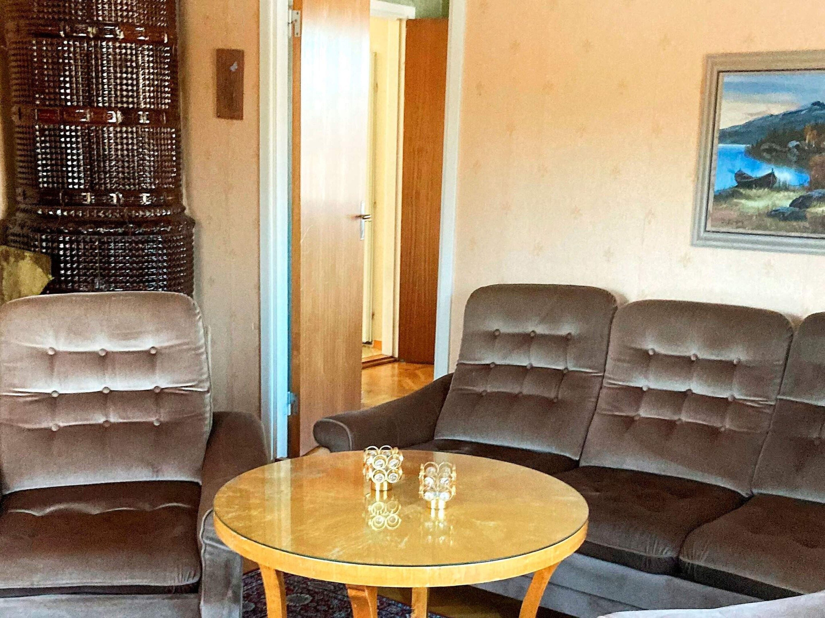A room with a sofa set, a glass coffee table, and a painting on the wall.