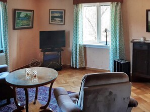 Olohuone, jossa on televisio, sohva, lasinen sohvapöytä ja kuviollinen matto.