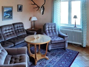 Un salon comprenant un ensemble de canapés, une table basse ronde, une lampe et un crâne de cerf accroché au mur.