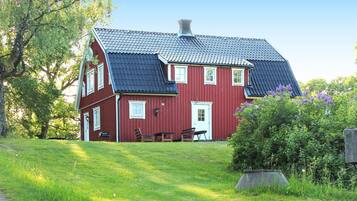 A red wooden house with a sloped roof, a front porch, and a small garden area.