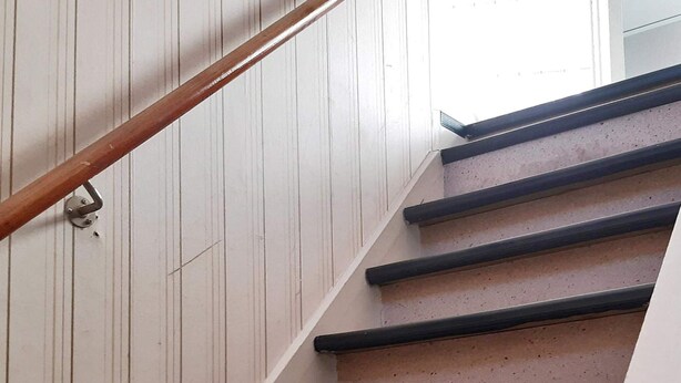 Eine Treppe mit einem hölzernen Geländer und einer weißen Wand mit vertikalen Linien.