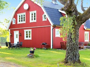 A red wooden house with a sloped roof, a large tree in front, and a grassy yard. - 7 Person Holiday Home in Oxaback (Öxabäck)