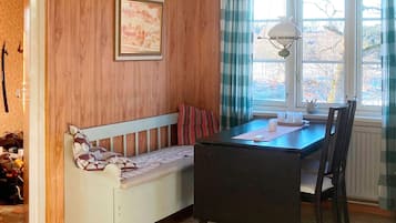 A room with a wooden wall, a bench, a table with chairs, and a window with curtains.