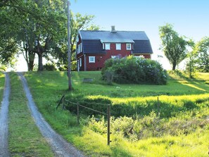 Punainen talo, jossa on harmaa katto, ja sen ympärillä on ruohikkoista peltoa ja puita.