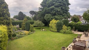 A well-maintained garden with a lawn, various shrubs, and a patio area with outdoor furniture. - Unwind in Comfort at Cosy Caradus Free Parking (Birmingham)