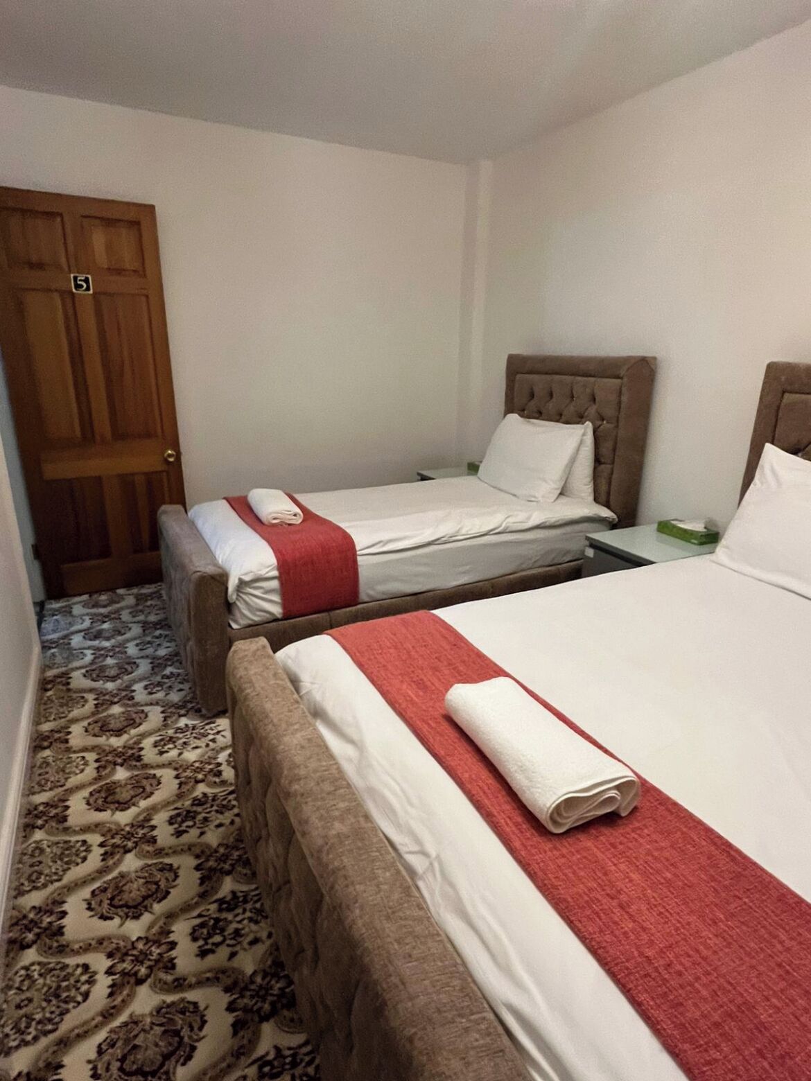 A hotel room with two beds, a wooden door, and patterned carpet.