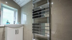 A modern bathroom with a white sink, chrome towel racks, and a window with blinds. - Chapel Lodge by Tŷ SA (Newport)