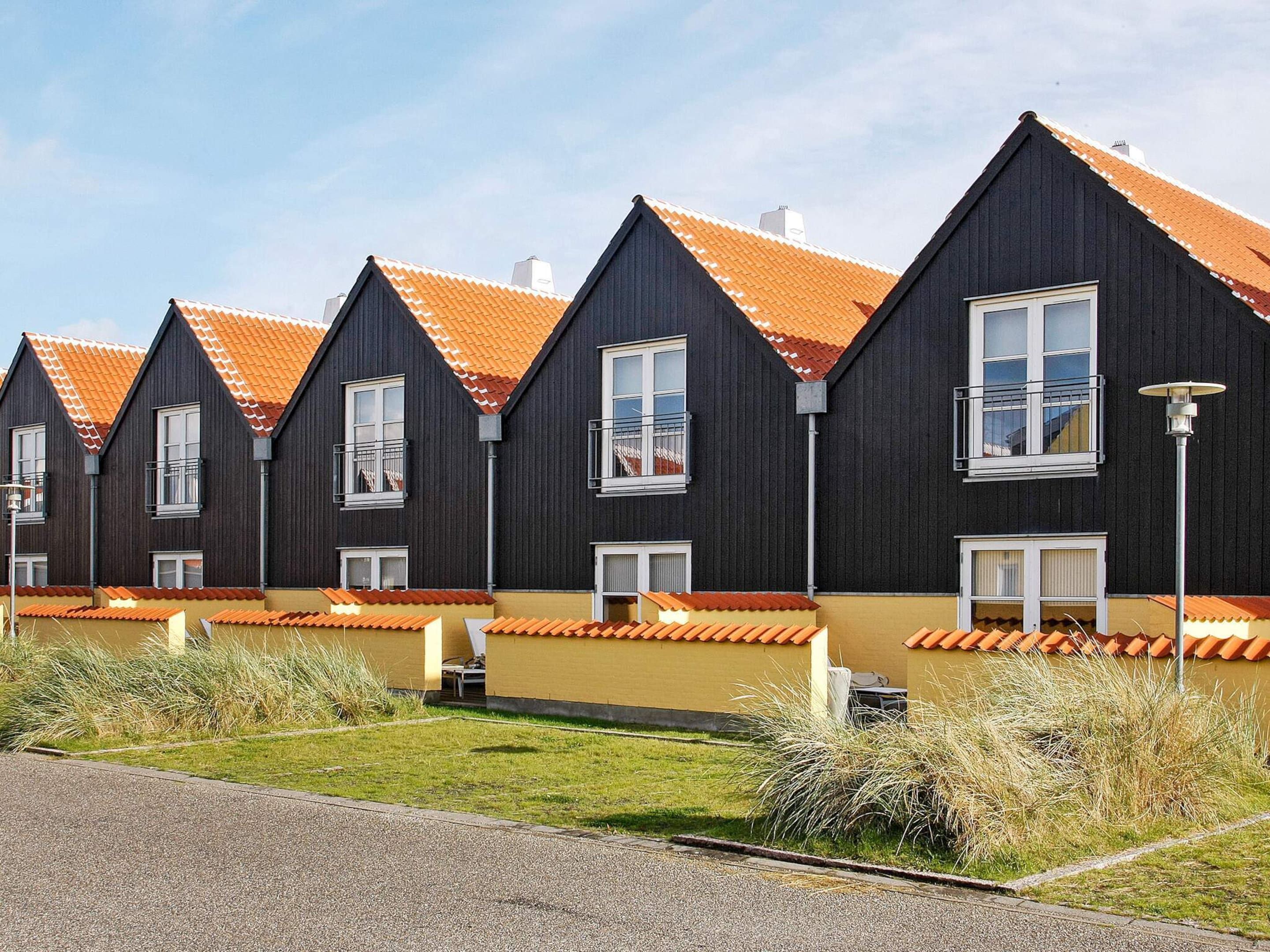 A row of modern, dark-colored houses with orange-tiled roofs and white-framed windows.