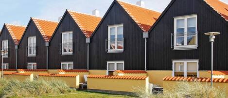 A row of modern, dark-colored houses with orange-tiled roofs and white-framed windows.
