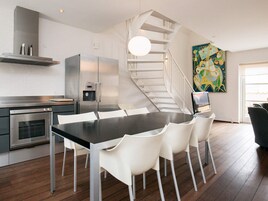 Una cocina moderna con electrodomésticos de acero inoxidable, un comedor con mesa negra y sillas blancas, y una escalera en espiral que lleva a un nivel superior.