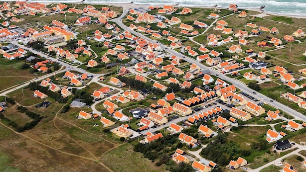 Una vista aerea di una zona residenziale costiera con case dai tetti arancioni, disposte a griglia lungo la costa.