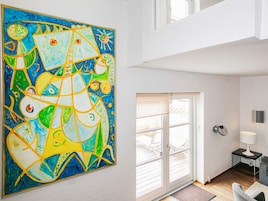 Una habitación con un cuadro abstracto grande en la pared, una puerta corrediza de vidrio que da a un espacio exterior y una mesita con una lámpara.