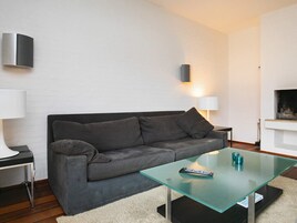 A modern living room with a grey sofa, a glass coffee table, a remote control, and a fireplace.