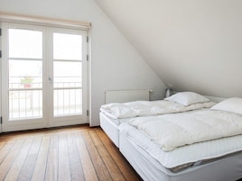 Un dormitorio con techo inclinado, una cama con ropa de cama blanca, un radiador y una ventana con vista al exterior.